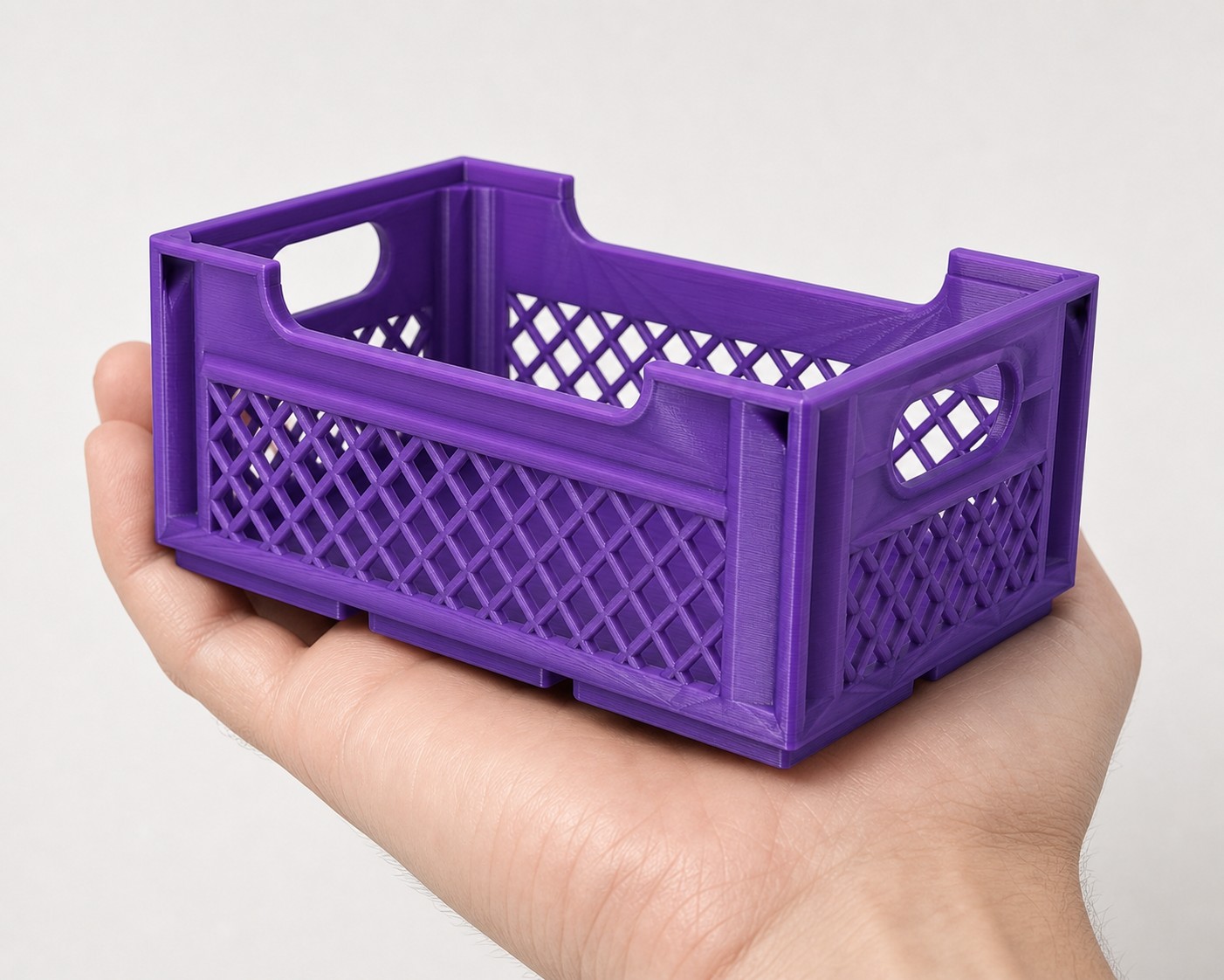A purple printed Gridfinity crate held in an open palm, showing the milk-crate lattice walls and stacking rim